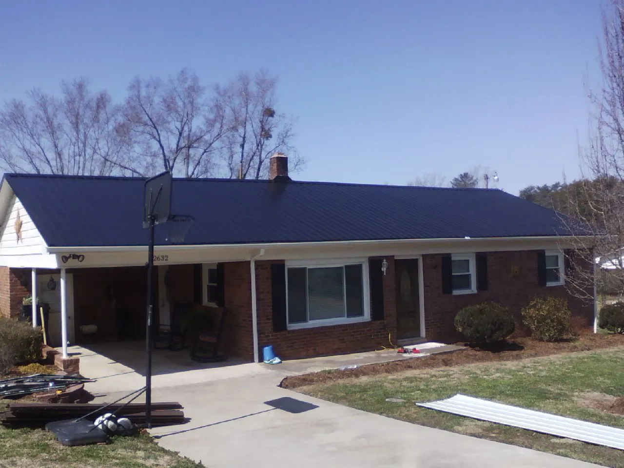 Finished dark blue metal roof on a brick ranch with a carport in Buckner