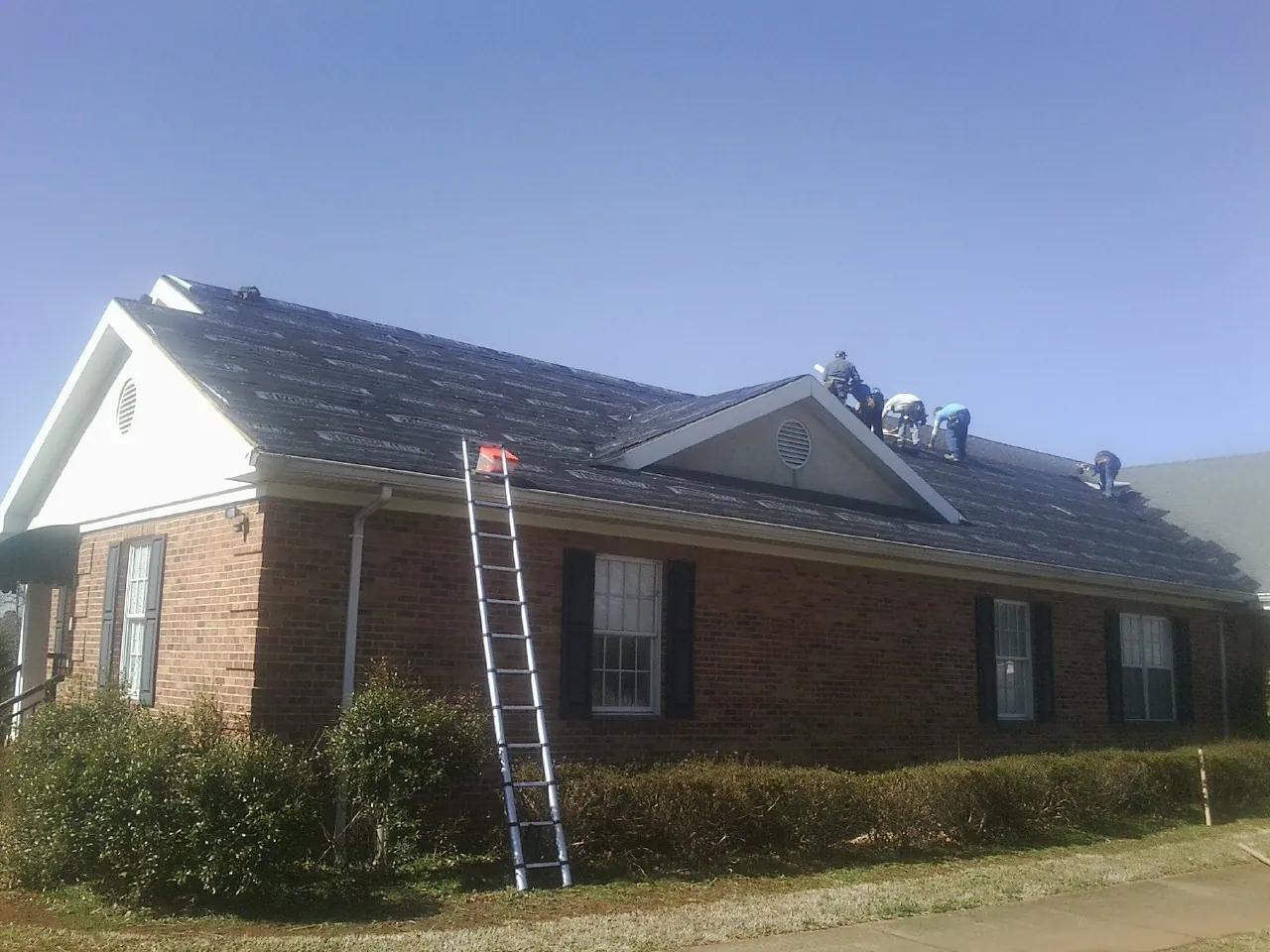 Crew tearing shingles off a brick ranch roof with a ladder set — Emergency Roof Repair work by our crew in Buckner