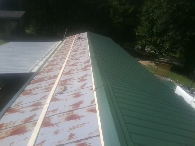 Old rusted panels beside newly installed green metal roofing — Wind Damage Roof Repair by Roofing Brothers in Buckner