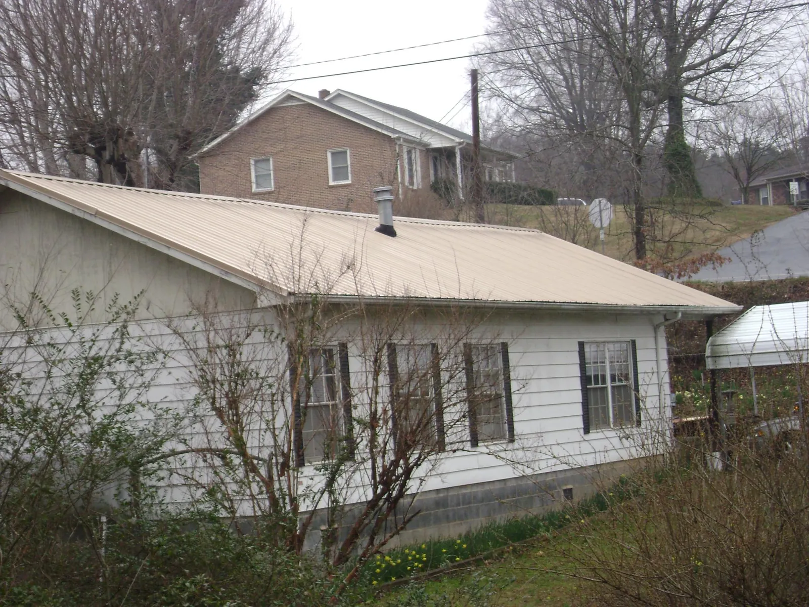 Tan metal roof on a white sided house set into a hillside — Commercial Roofing by Roofing Brothers in Buckner